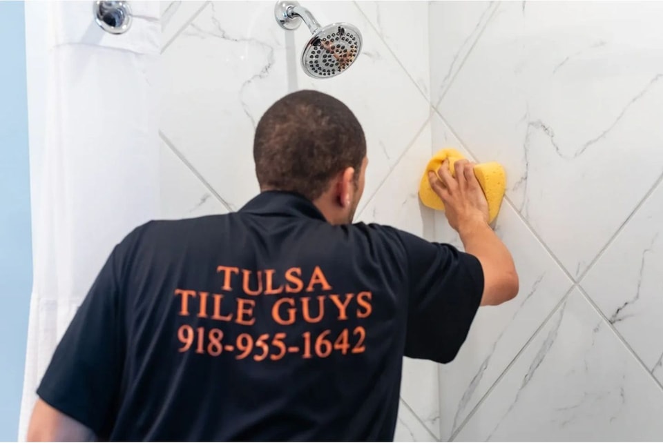 Craftsman sponging grout from a marble-look tile shower wall