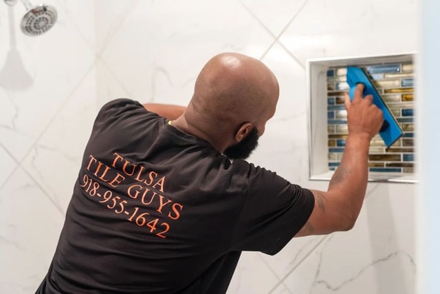 Craftsman grouting a blue glass mosaic shower niche with a grout float