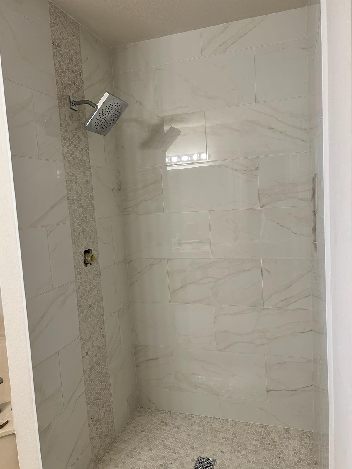 Large-format marble tile shower with modern square showerhead and vertical hex accent
